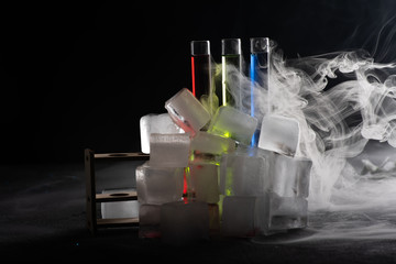 Colorful shot drinks in glass tubes with smoke or steam around and bunch of ice cubes. Dark background, atmospheric bar image