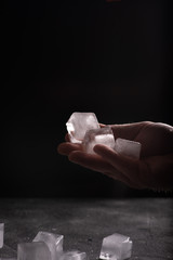 Man's hand holding a bunch of ice cubes, scattered ice on a table. Atmospheric dark image