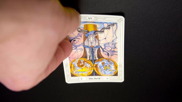 A hand lays out a tarot card, Thoth Tarot, "The Devil" on black tablecloth. Tokyo, Japan. March, 2020. Camera fixed, close-up, high angle view.