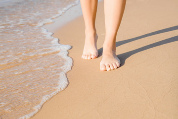 Young woman barefoot walking on beach at sea in sunny summer day. Restful moment. Part of body. Front view. Closeup.