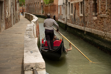 Gondolero y góndola en soledad en uno de los numerosos canales de la ciudad italiana de Venecia. - obrazy, fototapety, plakaty