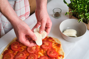 A man is preparing pizza. Cooking homemade italian pizza. Preparation raw ingredients for baking. Sauce, tomatoes and cheese. Fresh natural healthy food. Сulinary сhef kneading dough on kitchen table