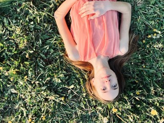 a skinny teenage girl in light summer dress lying on green grass