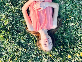 a skinny teenage girl in light summer dress lying on green grass