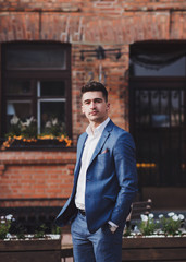 Handsome young brunette model, wearing suit, looking at camera, posing in city. Business man portrait. 