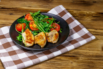 Fried chicken breast with salad of fresh arugula and cherry tomatoes on wooden table