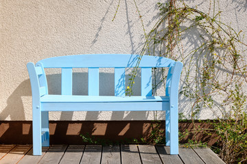 Beautiful wooden garden bench painted in light blue standing in front of a house wall on a terrace on a sunny springtime day. Seen in Germany in April.