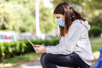 bambina con i capelli neri indossa una mascherina facciale per proteggersi usa un tablet al parco