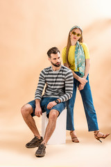 fashionable couple posing in summer clothes on white cube on beige