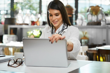 Young attractive brunette elegantly dressed sitting in restaurant and preparing to work on laptop.