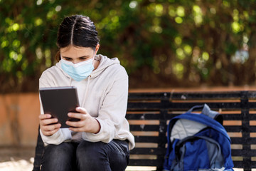 Fototapeta premium bambina con i capelli neri indossa una mascherina facciale per proteggersi usa un tablet al parco 