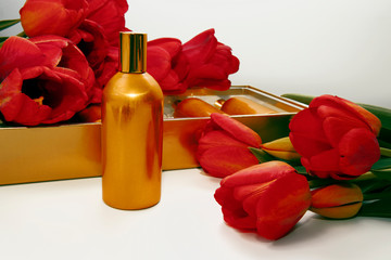 A golden bottle stands on the background of a gift box and red tulips.