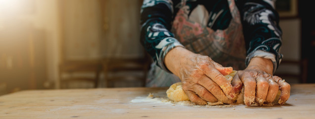 Close up of old woman hands kneading dough to prepare handmade pasta on a wooden cutting board....