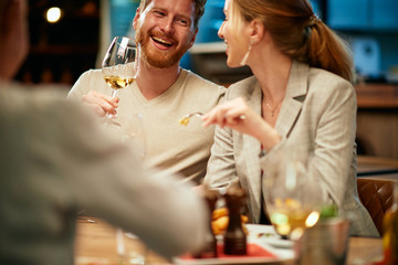 Couple sitting in restaurant with friends, chatting, drinking and eating dinner.