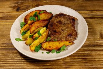 Fried beef steak with potato wedges on wooden table