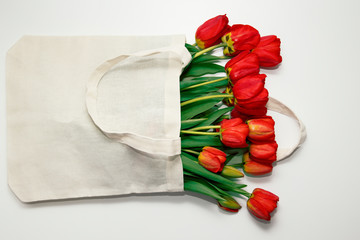 Red tulips lie inside of eco-bag on a white surface.