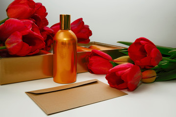 An open envelope lies in the background of a golden bottle and red tulips.