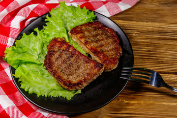 Grilled pork steaks with lettuce leaves on wooden table. Top view