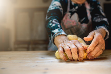 Close up of elderly woman hands kneading dough to prepare handmade pasta on a wooden cutting board. Free space for text on the left.