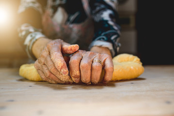 Close-up of old floured hands kneading dough to prepare fresh homemade pasta on a wooden cutting board. Italian old woman.