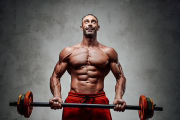 Handsome adult sportsman wearing sportswear posing for a camera while holding a barbell