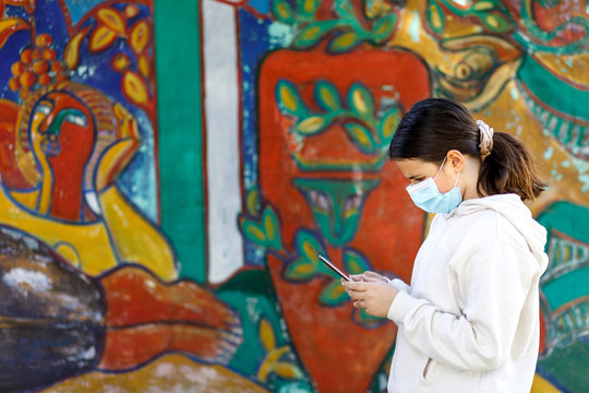 Adolescente con una mascherina con un mascherina chirurgica utilizza il tablet , isolata su sfondo murales