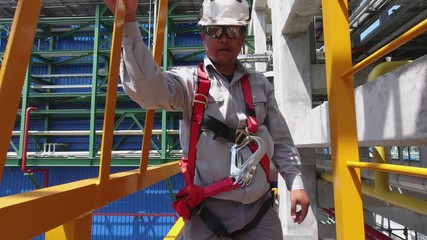 Engineers wear a full body safety harness and climb up the vertical ladder in an industrial factory to check the condition of the equipment.