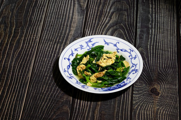 Fried Malabar spinach and egg on white porcelain plate with beautiful blue pattern on wooden table. Chinese dish. Asian dish. Macro.
