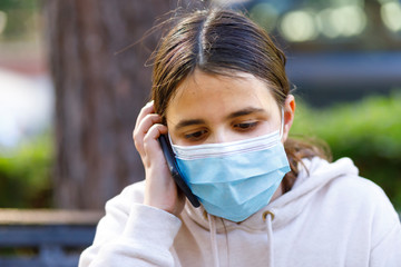 bambina con i capelli neri indossa una mascherina facciale per proteggersi utilizza uno smartphone per fare una chiamata ,  isolata su sfondo natura