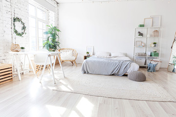Stylish loft bedroom interior. Spacious design apartment with light walls large windows big bed. Clean modern decoration with elegant furniture in minimalist Scandinavian style.