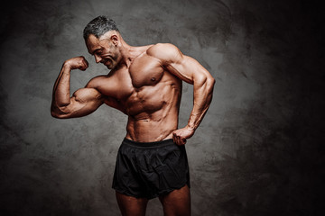 Fototapeta premium Shirtless adult male bodybuilder showing his biceps in a dark studio