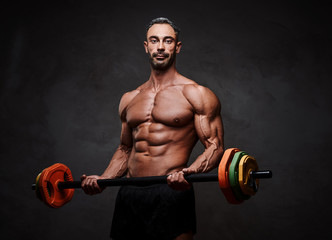 Fototapeta na wymiar Shirtless adult male bodybuilder doing a biceps exercise with a barbell in a bright studio