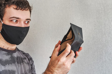 Portrait of a shocked, surprised man in black mask, executive holding and looking into his empty wallet. Bankruptcy financial difficulties concept against the background of the pandemic