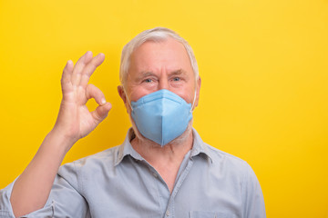 Handsome senior man in medicine mouth mask showed sign OK