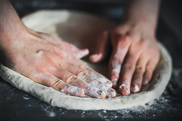 Making dough for homemade pizza with the bare hands. The dough is on a black baking sheet. Home...
