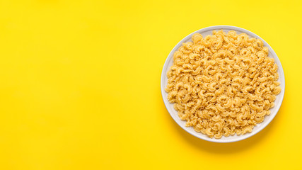 many dry unprepared pasta - cockerels on a beige plate on a yellow background