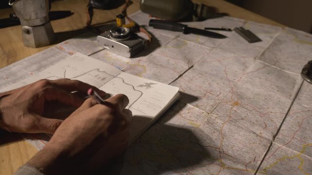 Man drawing map on his rustic table with camping accessories