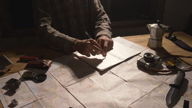 Man drawing map on his rustic table with camping accessories