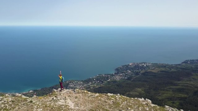 Woman stands near the cliff of the highest mountain in Crimea - Ai-Petri and raises her arms to the sides against the backdrop of the Black Sea and forests, imagining that she is flying over the city.