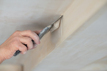 Worker putsty plasterboard ceiling in new building. Repairman works with plasterboard, plastering dry-stone wall, home improvement. A man makes repairs at home. Putty knife in male hand