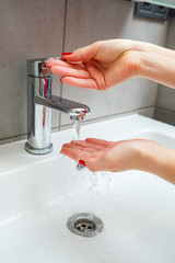 White sink with a silver faucet in the bathroom. Gray can with liquid soap for hands. Turning on the tap water, personal hand hygiene. Hand washing under running water