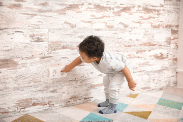 Little African-American baby playing with socket at home. Child in danger