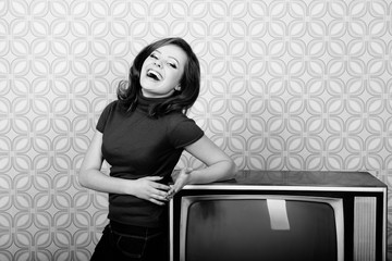 Young charming woman staing at room with vintage wallpaper and retro TV set, retro stylization...