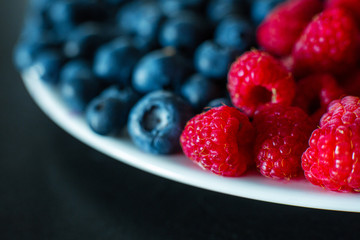 A close-up of raspberries and black blueberry split the frame. Summer vitamins