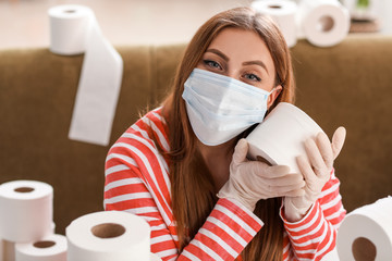 Woman in protective mask and with heap of toilet paper at home. Concept of coronavirus epidemic