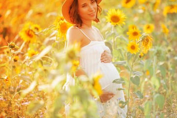 Obraz na płótnie Canvas Beautiful young pregnant woman in the sunflower field. Portrait of a young pregnant woman in the sun. Summer.