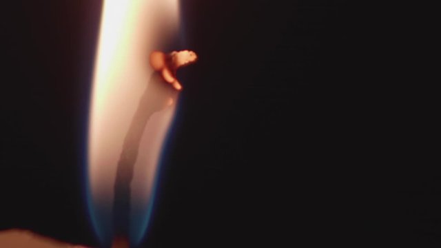 Close up view on candlle burning in darkness. High steady flame barely moves above the paraffin.