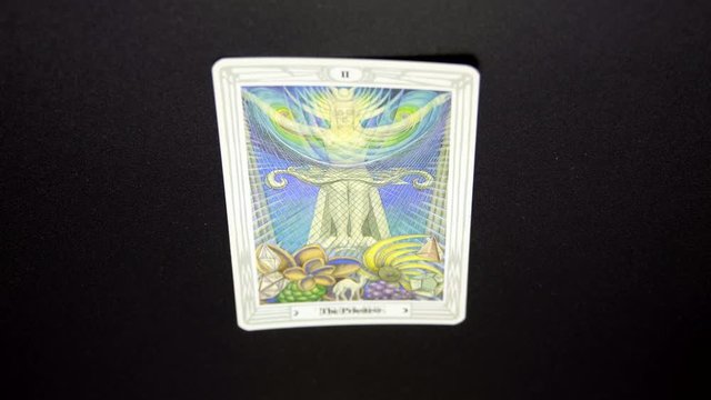 A hand lays out a tarot card, Thoth Tarot, "The Priestess" on black tablecloth. Tokyo, Japan. March, 2020. Camera fixed, close-up, high angle view.