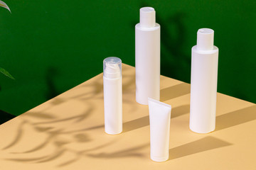 White plastic skincare tubes on a background of tropical plant shadow with copy space