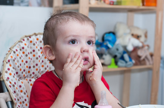 A Little Boy In A Red T-shirt On A High Chair Eating Macaroni With His Hands